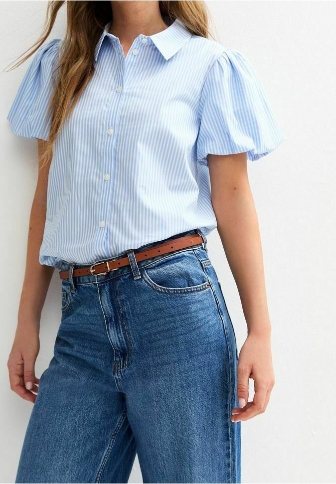 Femme portant un chemisier à manches courtes rayé bleu clair et blanc avec des manches bouffantes, rentré dans un jean bleu taille haute avec une ceinture marron.