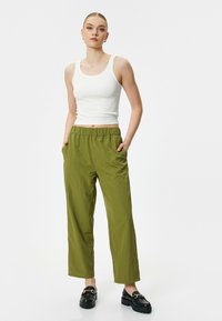 Groene, lichte, losvallende broek met een elastische tailleband en twee zijzakken, gecombineerd met een witte tanktop en zwarte schoenen.