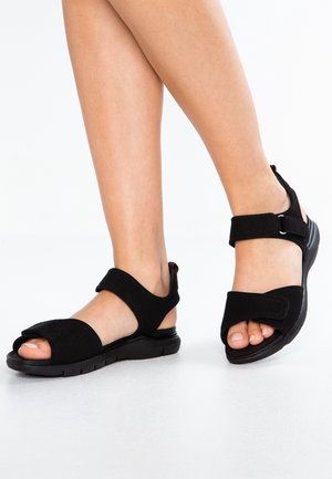 Sandalias negras con acabado de gamuza, con dos correas ajustables de gancho y bucle y diseño de punta abierta, montadas sobre una suela negra.