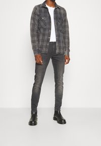 Graues kariertes Flanellhemd über einem weißen T-Shirt, kombiniert mit dunklen Jeans und schwarzen Chelsea-Stiefeln. Verfügt über Vordertaschen und Knopfleiste.