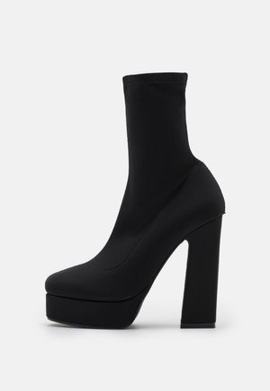 Czarne botki na platformie z dopasowaniem przypominającym skarpetę, wyposażone w masywny obcas i gładką teksturę. Smukły, opływowy design bez żadnych zdobień.