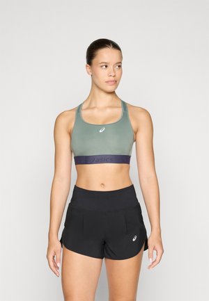 Soutien-gorge de sport vert avec une bande inférieure marine arborant le logo "asics" ; associé à un short de course noir, en tissu lisse et avec un design épuré.