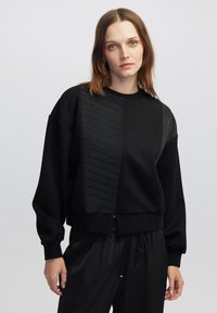 Schwarzer Sweatshirt mit strukturiertem Einsatz, weiten Ärmeln und geripptem Saum. Hergestellt aus weichem Stoff, mit horizontalen Linien und lässiger Passform.