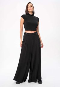 Zwarte cropped top met hoge hals, gecombineerd met zwarte wijde pijpenbroek met een riem en geplooid ontwerp. Gladde stoftextuur.