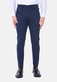 Chino blu navy con vestibilità slim, realizzati in tessuto di cotone, con chiusura frontale a bottone e tasche. Indossati con scarpe nere.