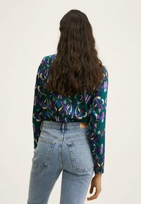 Blusa a maniche lunghe con un motivo floreale multicolore su uno sfondo scuro; abbinata a jeans in denim azzurri a vita alta.