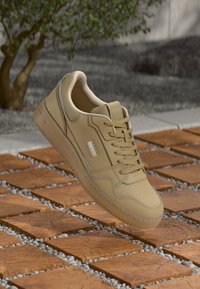 Beige Leder-Sneaker mit perforiertem Zehenbereich, strukturierten Seiten und Schnürdesign. Leichte Sohle mit dezenten Nähakzenten.