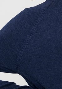 Camicia a maniche lunghe blu navy, realizzata in tessuto morbido, con scollatura rotonda e design senza cuciture sulle spalle, che mostra un primo piano della texture.