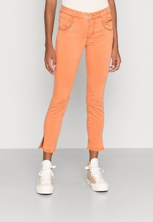 Perzikkleurige cropped jeans met een gladde textuur, ritszakken en zijsplitten aan de zoom, gecombineerd met witte hoge sneakers.