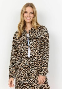 Leopard print jacket featuring a soft material, button closures, two chest pockets, and a relaxed fit, paired with a white top and matching skirt.