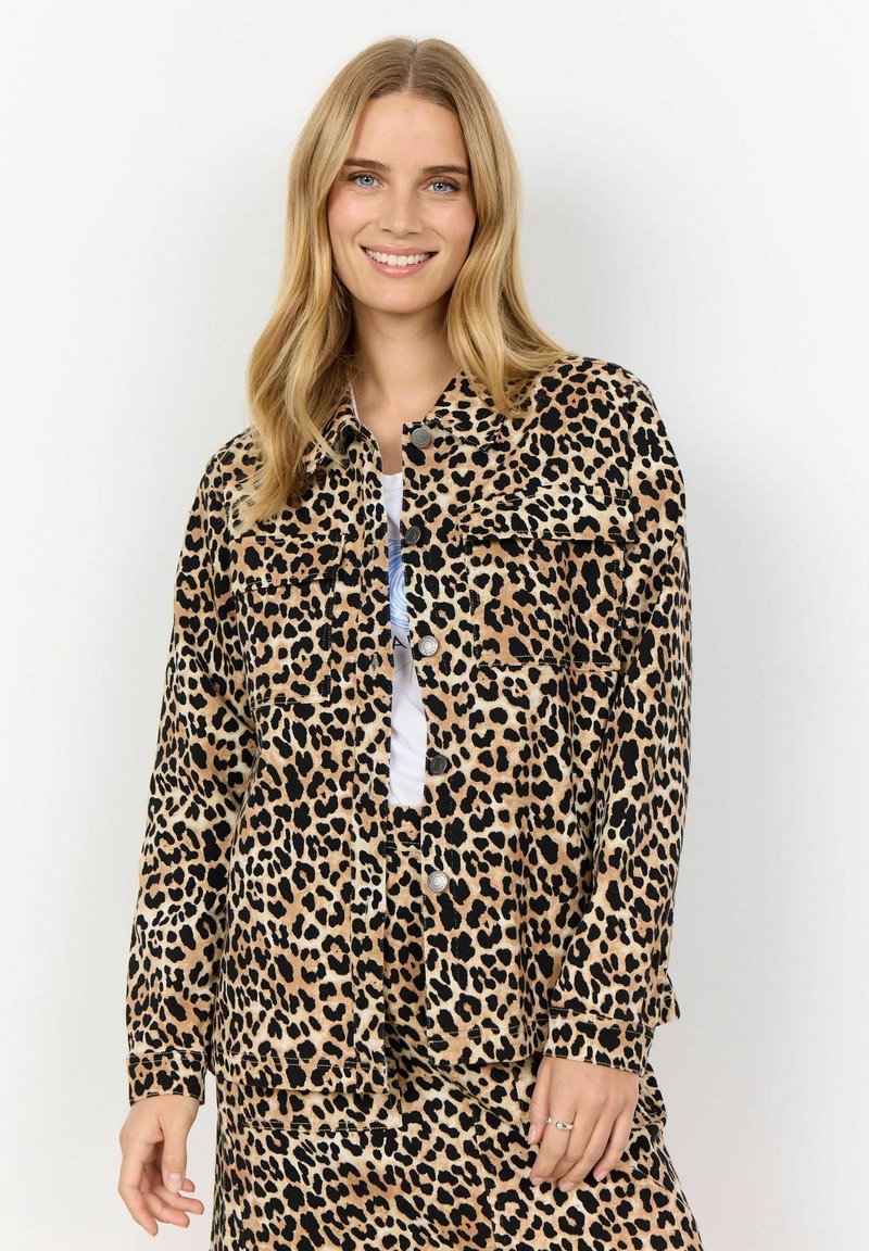 Leopard print jacket featuring a soft material, button closures, two chest pockets, and a relaxed fit, paired with a white top and matching skirt.