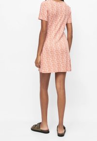 Vestido de manga corta en naranja con estampado floral blanco, hecho de una tela suave; tiene un corte holgado y un dobladillo acampanado. Se lleva con sandalias planas.