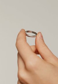 Anillo de plata sostenido entre los dedos, con una superficie lisa y pulida y un sutil grabado de corazón en la parte interior de la banda.