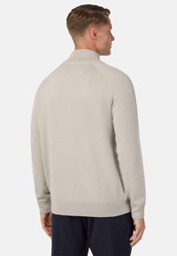 Jasnoszary sweter z wysokim kołnierzem, prążkowanymi mankietami i dołem. Gładka textura i dopasowany fason z raglanowymi rękawami, widoczny z tyłu.