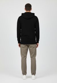 Felpa nera con tasca a marsupio frontale, polsini e orlo a coste, abbinata a pantaloni beige chiaro e sneakers bianche. Texture del tessuto liscia.