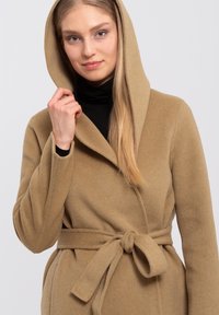 Beige wool coat with a hood, featuring a wrap design and tied belt at the waist. Soft texture and subtle stitching details.