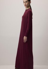 Longue robe bordeaux en tissu lisse, avec des manches longues et un col rond, conçue avec une silhouette droite.