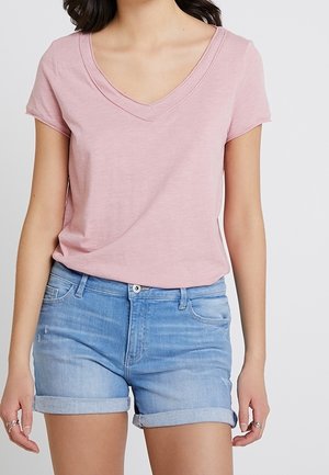 Różowy T-shirt z dekoltem w serek i krótkimi rękawami, wykonany z miękkiej tkaniny. W połączeniu z jasnoniebieskimi, podwiniętymi szortami dżinsowymi z przednimi kieszeniami.