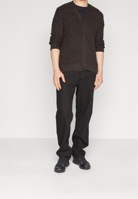Cardigan a maglia marrone con scollo a V e sei bottoni, abbinato a pantaloni neri a gamba dritta e scarpe da ginnastica nere. Design semplice e testurizzato.