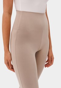 Beżowe legginsy z wysokim stanem o gładkiej, elastycznej fakturze i subtelnym połysku, z bezszwowym designem i bez widocznych zapięć.
