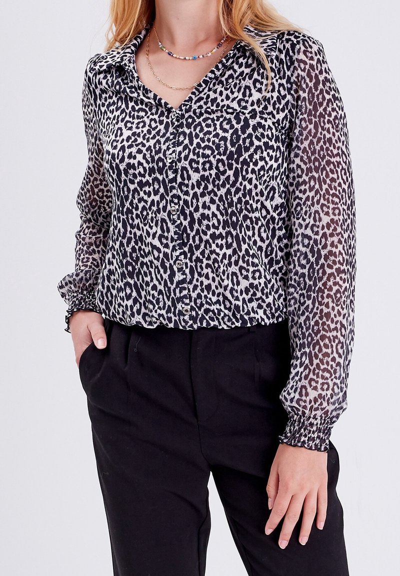 Leopardenmuster-Bluse aus transparenter Stoff mit Knopfleiste und Kragen. Sie hat lange, geraffte Ärmel und eine lockere Passform, kombiniert mit schwarzen Hosen.