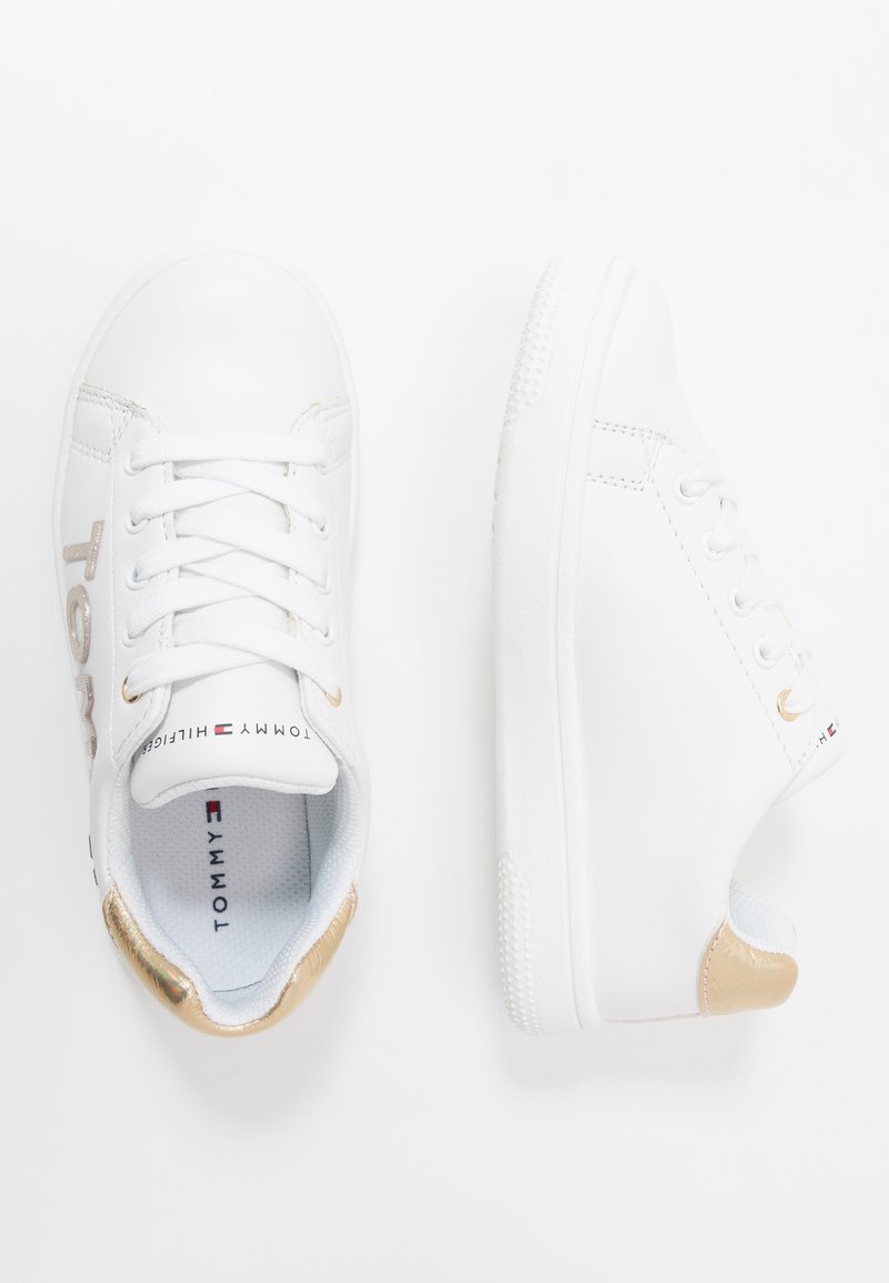 Zapatillas blancas de material sintético, con un diseño de cordones en la parte delantera, detalles dorados en el talón y una suela de goma con patrón.