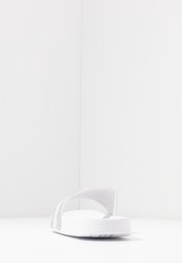 Infradito bianche con suola in gomma, dotate di due larghe cinghie trasparenti. Texture liscia e design minimalista.