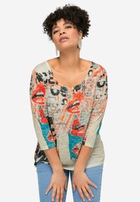 Haut à manches longues léger et multicolore avec un design graphique comprenant des lèvres, du texte et des motifs abstraits. Col en V et coupe ample.