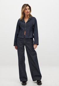 Marineblaue gestreifte Jeansjacke mit einem Reißverschluss auf der Vorderseite, kombiniert mit passenden weiten Hosen. Der Stoff hat eine glatte Textur und einen dezenten Glanz.