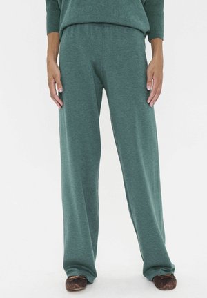 Grüne weit geschnittene Hosen aus weichem Strickstoff, mit einem elastischen Bund und einer lockeren Passform. Dazu schlichte braune Ballerinas.