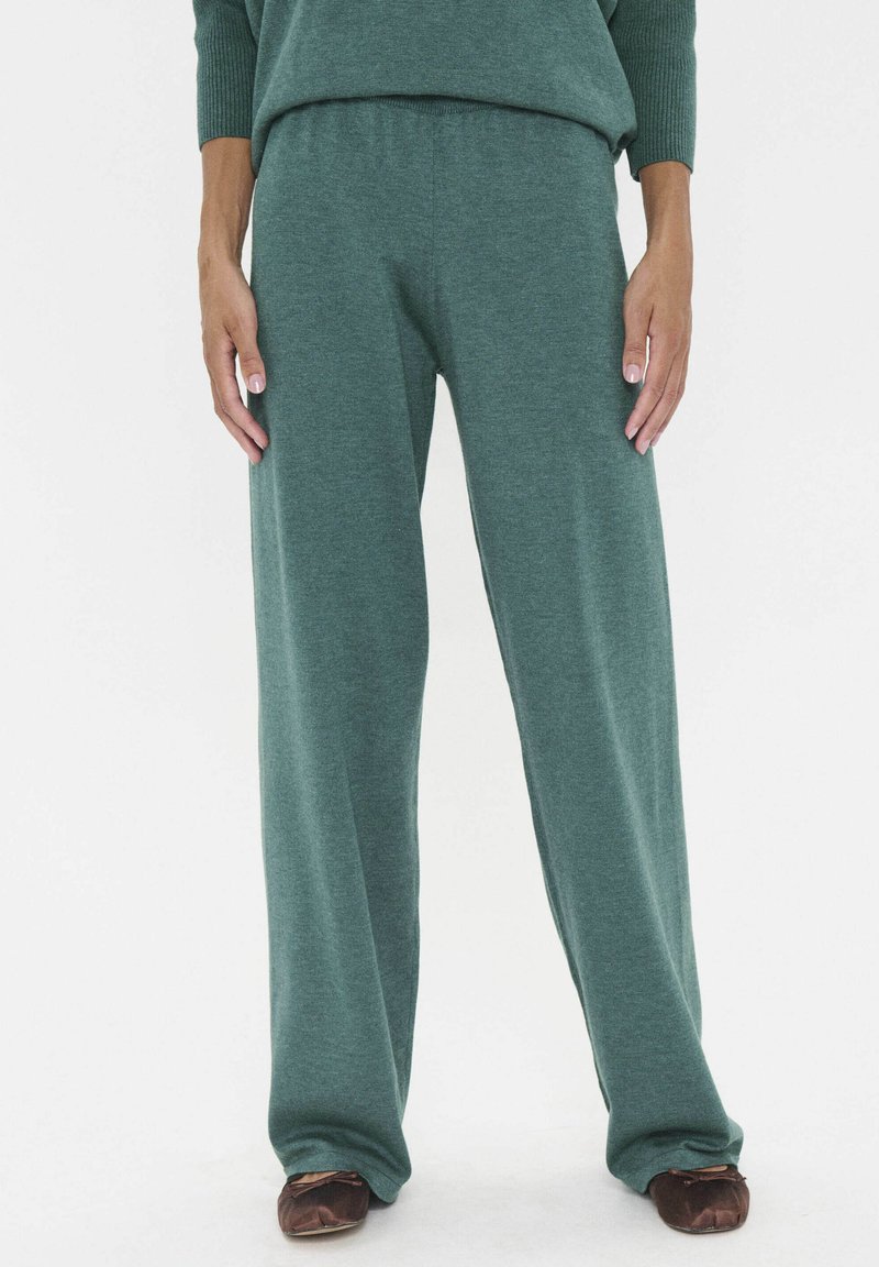 Grüne weit geschnittene Hosen aus weichem Strickstoff, mit einem elastischen Bund und einer lockeren Passform. Dazu schlichte braune Ballerinas.