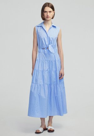  Lichtblauwe mouwloze jurk met een knoopsluiting kraag, voorste strikdetail, gelaagde ruffles en kleine patroonaccenten door de stof.