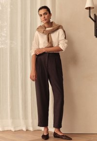 Hellfarbenes Hemd mit hochgekrempelten Ärmeln, braune strukturierte Hose und Leopardenmuster-Ballerinas. Ein beigefarbener Schal ist um den Hals gelegt.