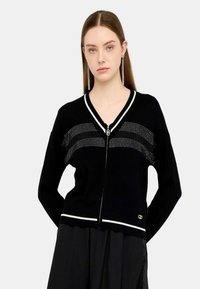 Cardigan lavorato a maglia nero con accenti bianchi, scollatura a V e chiusura con zip. Presenta un motivo a pois sulla parte anteriore e un dettaglio del logo sull'orlo.