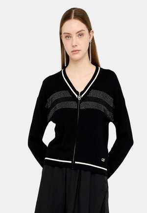Cardigan lavorato a maglia nero con accenti bianchi, scollatura a V e chiusura con zip. Presenta un motivo a pois sulla parte anteriore e un dettaglio del logo sull'orlo.