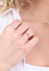 Zilveren ring met een golvend ontwerp, met een gepolijste afwerking. Handmatig weergegeven tegen een neutrale achtergrond, ter aanvulling van een witte blouse.