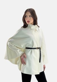 Capa blanca texturizada con un alto cuello, abrochada con un solo botón, ceñida en la cintura con un cinturón de cuero negro.