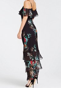 Svart blommig maxiklänning med volangärmar och lager av genomskinlig textur. Har färgglada blommönster och en figursydd bodice.