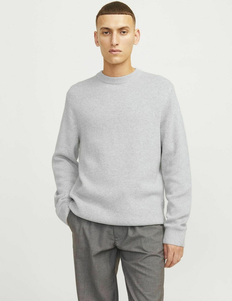 Grauer gestrickter Pullover mit Rundhalsausschnitt und langen Ärmeln, kombiniert mit grauen Hosen. Glatte Textur, minimalistisches Design ohne sichtbar Muster.