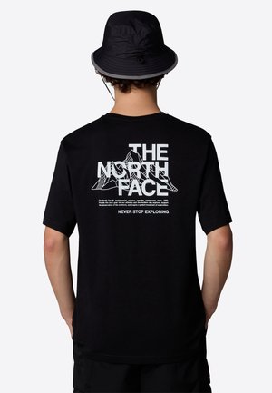 Osoba nosząca czarny kapelusz bucket oraz czarną koszulkę z białą grafiką góry i napisem "THE NORTH FACE" na plecach.