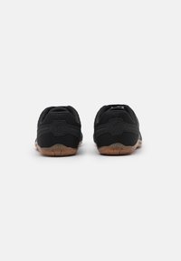 Een paar zwarte mesh sport schoenen met bruine zolen, getoond vanuit de achterkant op een witte achtergrond.
