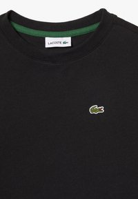 Mustapaitainen puuvillapaita, jossa on pyöreä kaula-aukko, vihreä sisäkauluksen reuna ja pieni brodeerattu krokotiillilogo vihreänä ja punaisena.