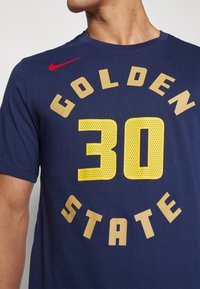 Námořnické modré tričko s žlutým sítotiskem "GOLDEN STATE" a "30" v kulatém designu; červené logo Nike na levém rameni.