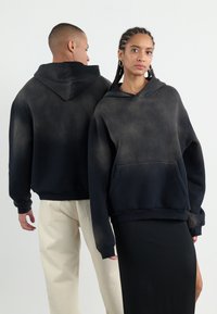 Haut à capuche noir surdimensionné avec un effet dégradé, capuche, poche avant et poignets côtelés. Porté par deux modèles de face et de dos.