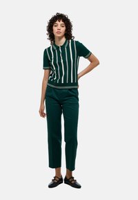 Polo shirt en tricot vert avec des rayures verticales blanches, manches courtes et col côtelé, assorti à un pantalon cropped vert et des chaussures noires.