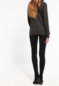 Felpa grigia scura con un fit rilassato, texture liscia e polsini a costine, abbinata a jeans neri attillati e stivaletti. Vista posteriore.