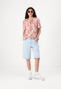 Rød og hvit mønstret kortermet topp med knyte-detall, sammen med lyseblå denimshorts og hvite høye sneakers.
