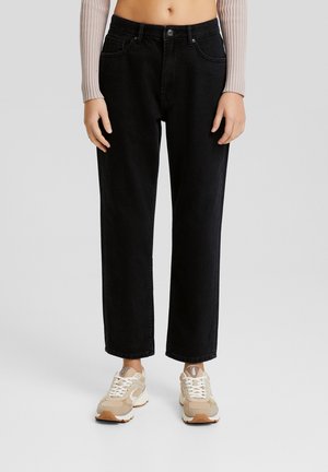 Jeans en denim noirs taille haute avec des jambes droites, design à cinq poches et couture contrastée. Portés avec des baskets de teinte neutre.