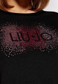 Zwarte T-shirt met het "LIU·JO" logo, versierd met een verloop van strass-steentjes in rood en zilver, wat een textuur en sprankelend effect creëert.