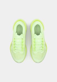 Zapatillas de correr verde claro con parte superior de malla, cordones planos y suela acolchada con un acento reflectante a lo largo del lado.